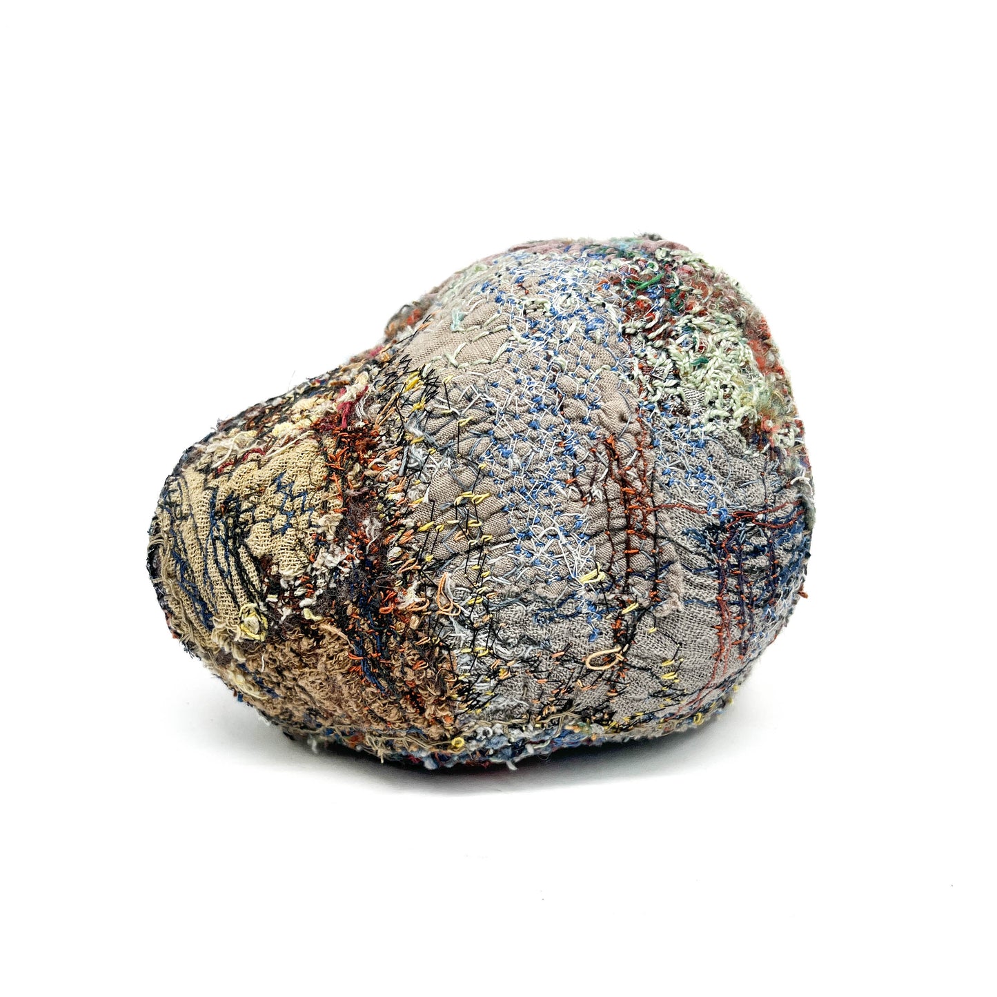 A textured stone showcases colorful and elaborate embroidery and stitching, creating a unique tactile surface.