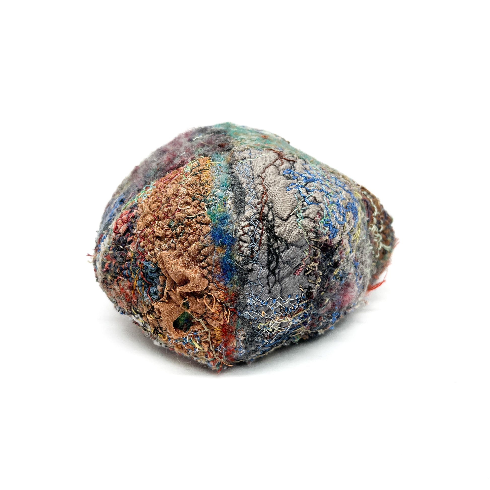 A textured stone displays a colorful and elaborate surface created by layers of embroidery and stitching.