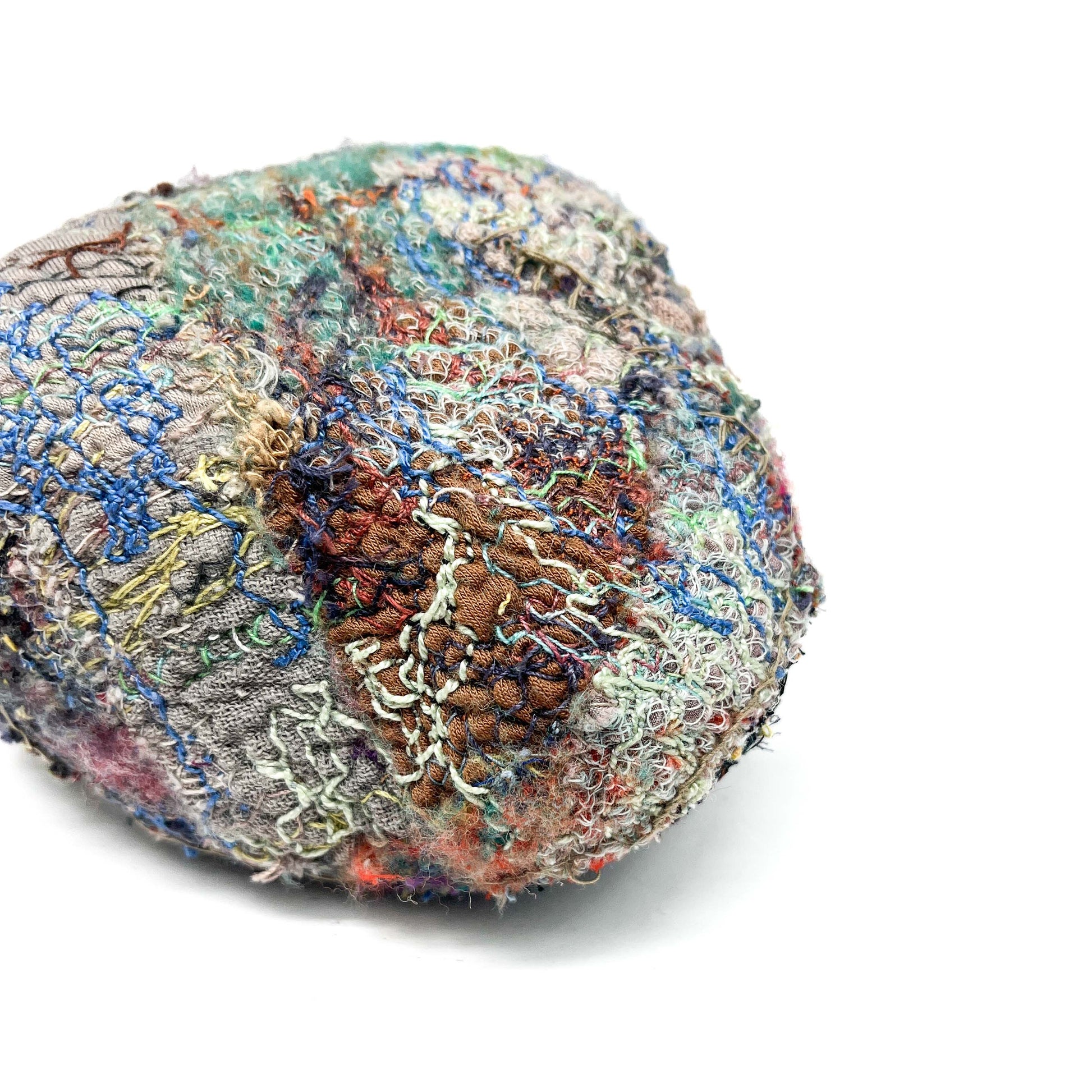 A textured stone features a detailed surface of colorful and intricate embroidery and stitching.