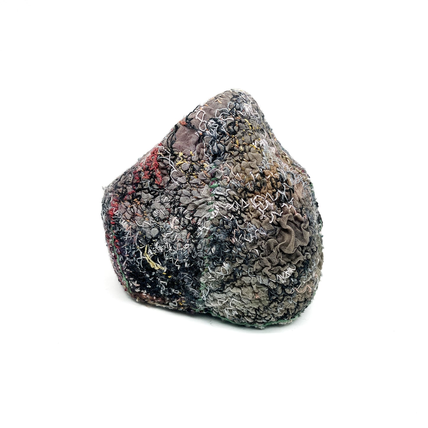 A textured stone showcases a surface covered in layers of colorful and intricate embroidery and stitching.