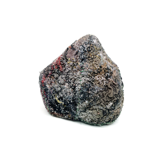 A textured stone showcases a surface covered in layers of colorful and intricate embroidery and stitching.