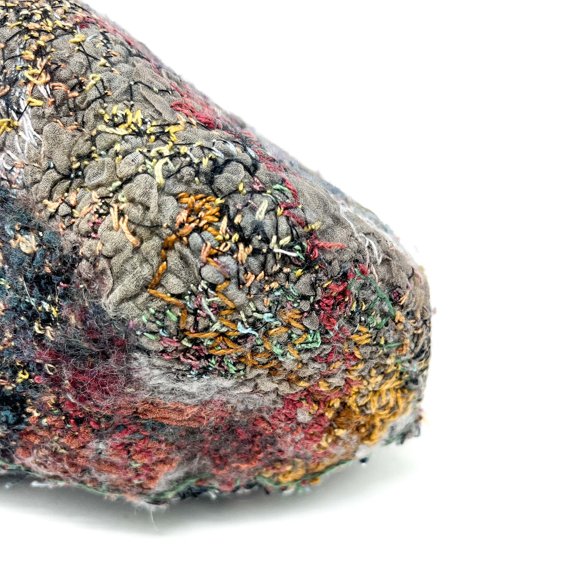 A close-up shows the textured surface of a stone covered in colorful and dense embroidery and stitching.