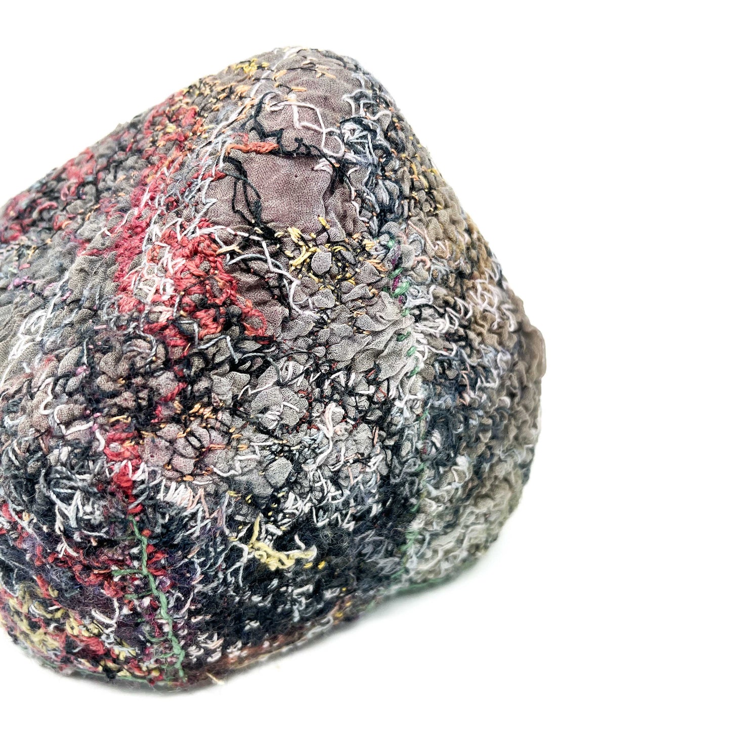 Textured, rounded object covered in dense embroidery with various thread colors and patterns.