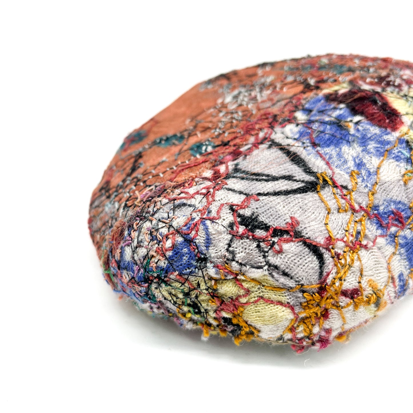 Textured, rock-like textile sculpture with intricate and colorful stitching details.