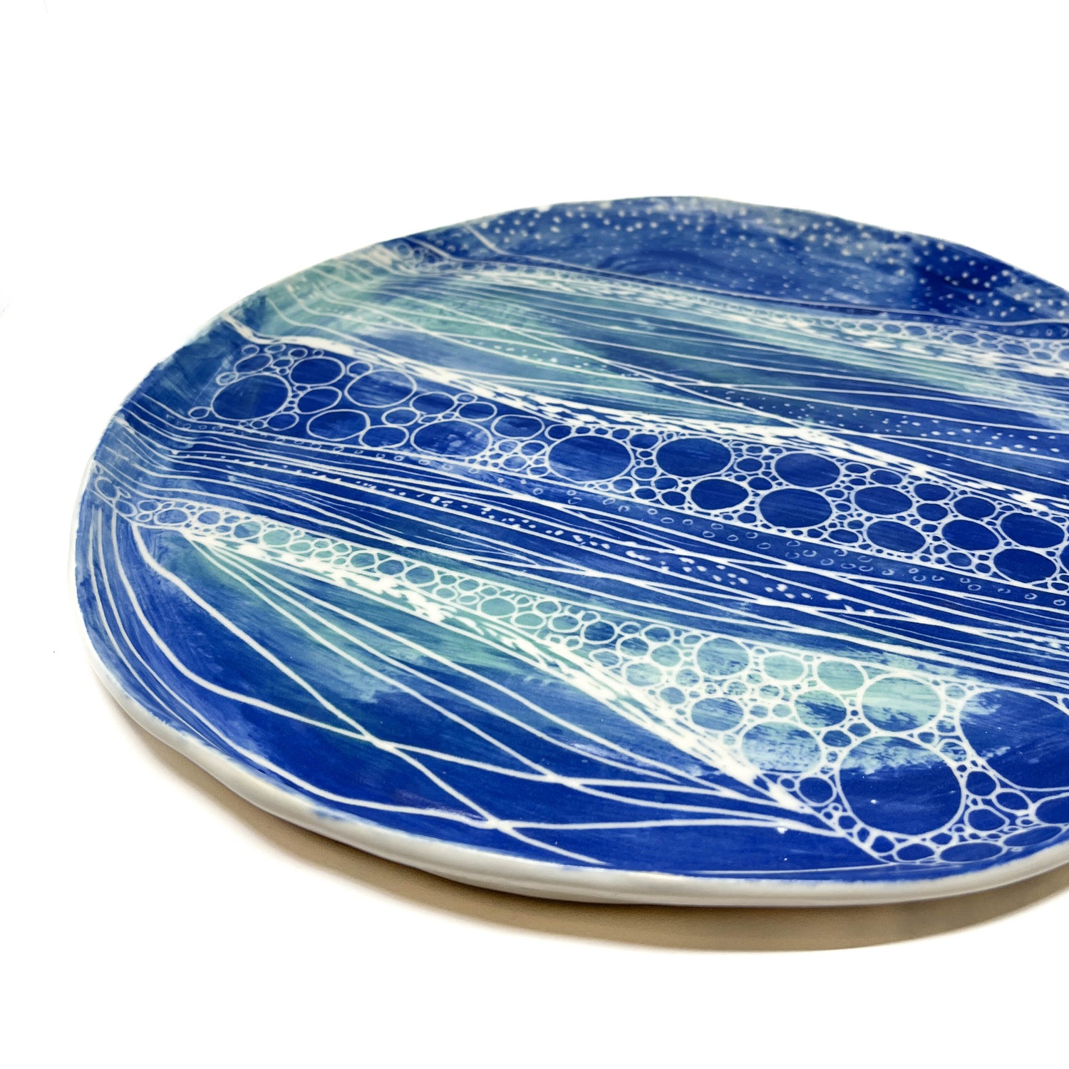 Angled view of a Round Salish Sea Platter, featuring a vibrant blue and teal swirl design with white details.