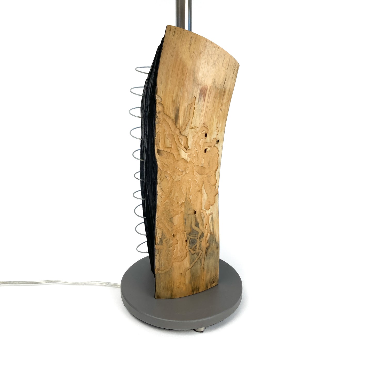Close-up of a lamp base made of natural wood with a charred blackened section and a metal spiral detail, mounted on a round stand.
