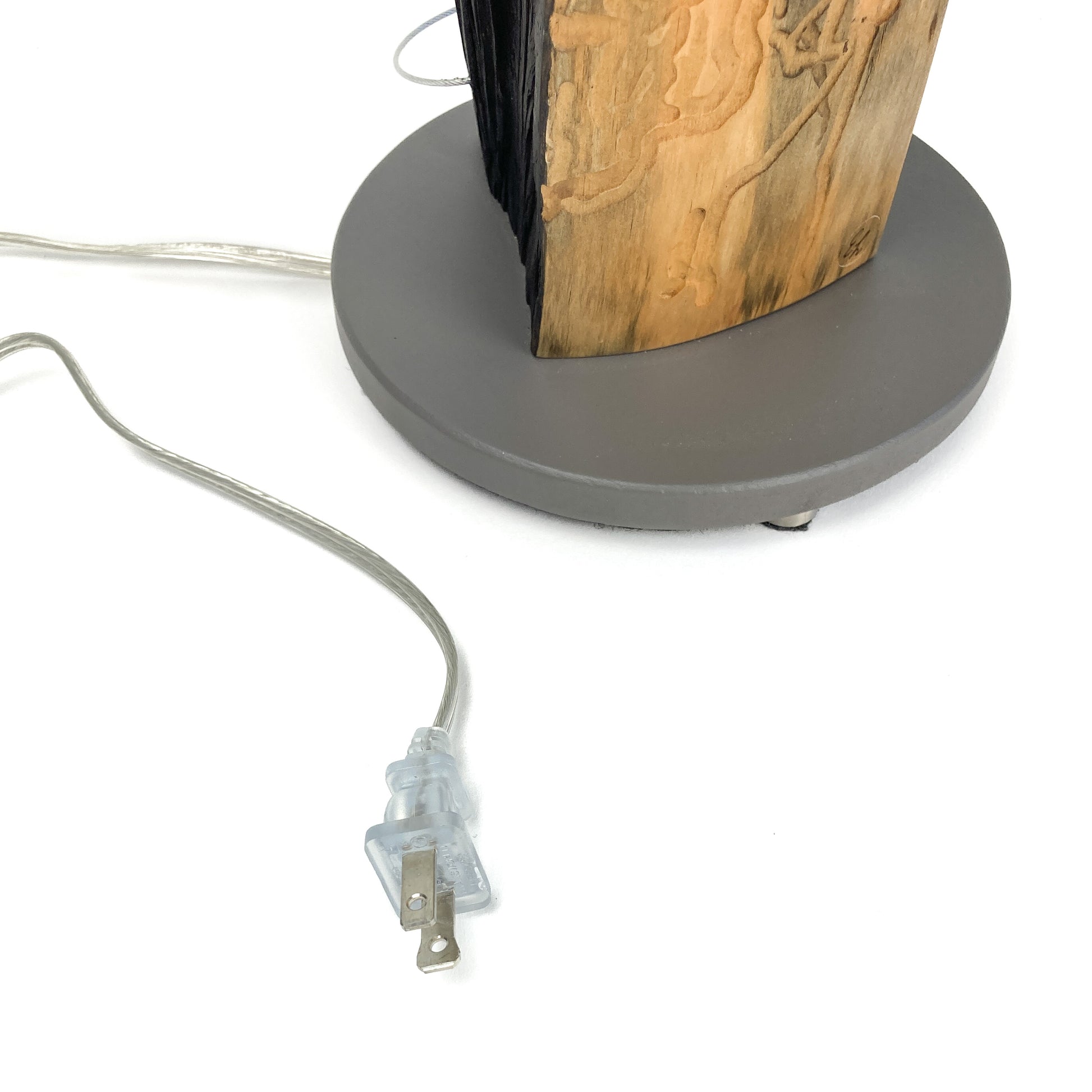 Close-up of a lamp base with a gray cord and clear plug on a white background. The lamp base is gray and round, and the lamp body is made of wood.