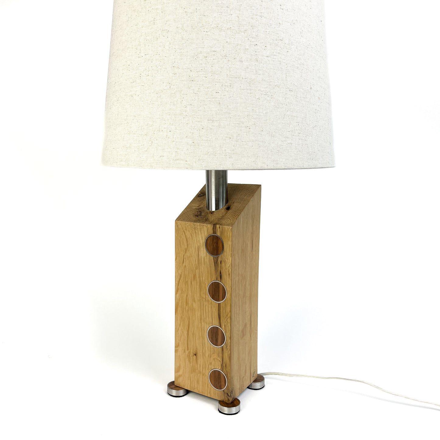 A table lamp with a light wood base, metal circles, white shade, and small metal feet.