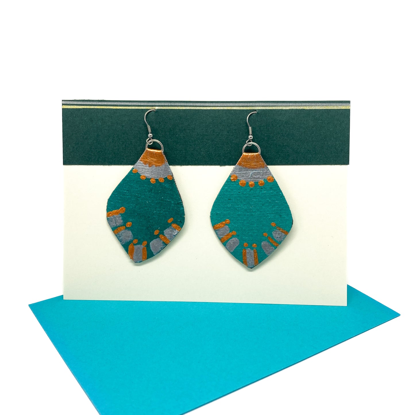 Two teal, copper, and silver geometric earrings with a leaf-like shape and linear details hang from silver hooks.