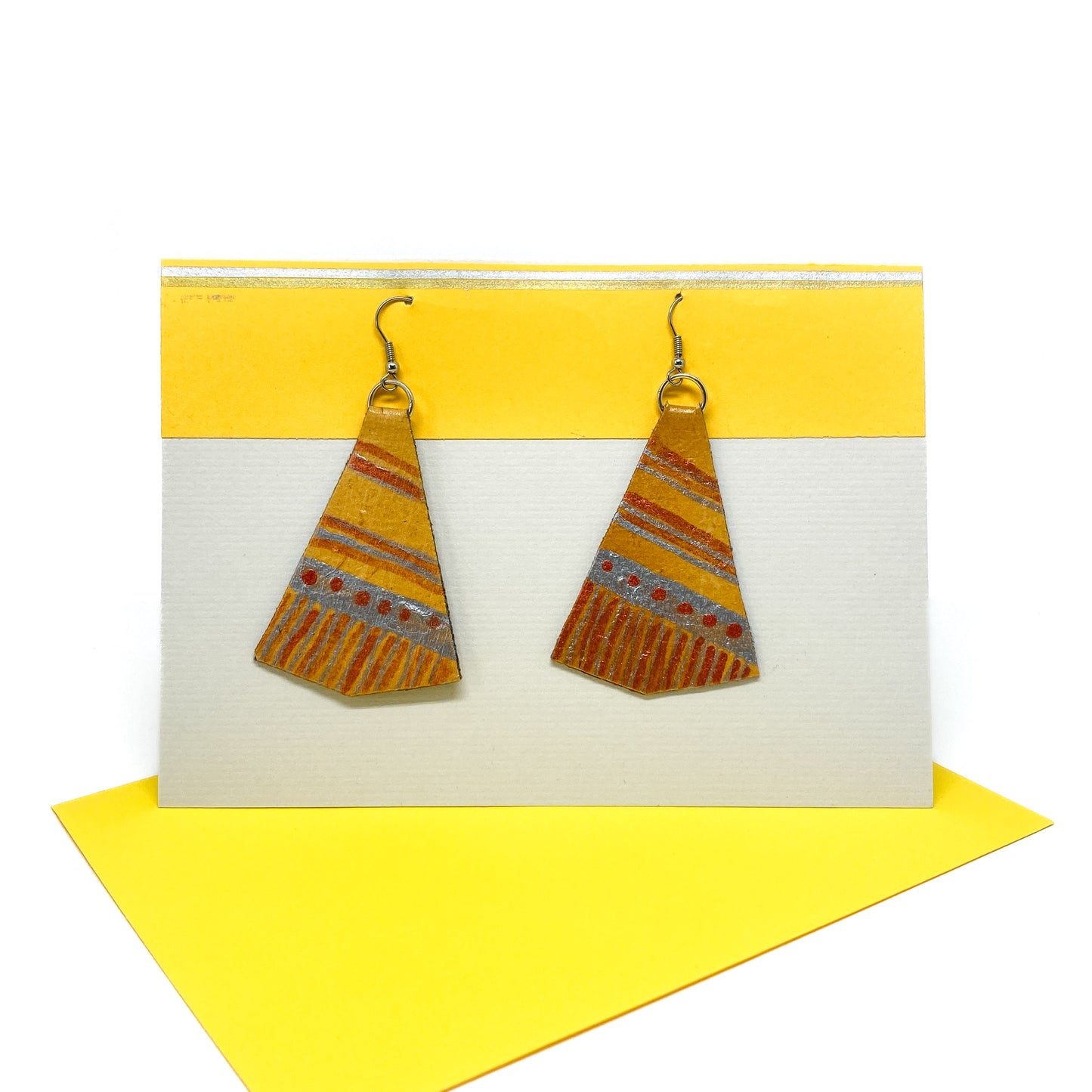 Two yellow, brown, and silver geometric earrings hang from silver hooks on a display card.