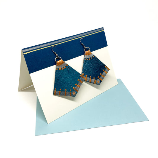 Folded greeting card with blue and gold stripes displaying geometric wood earrings, atop a light blue card.