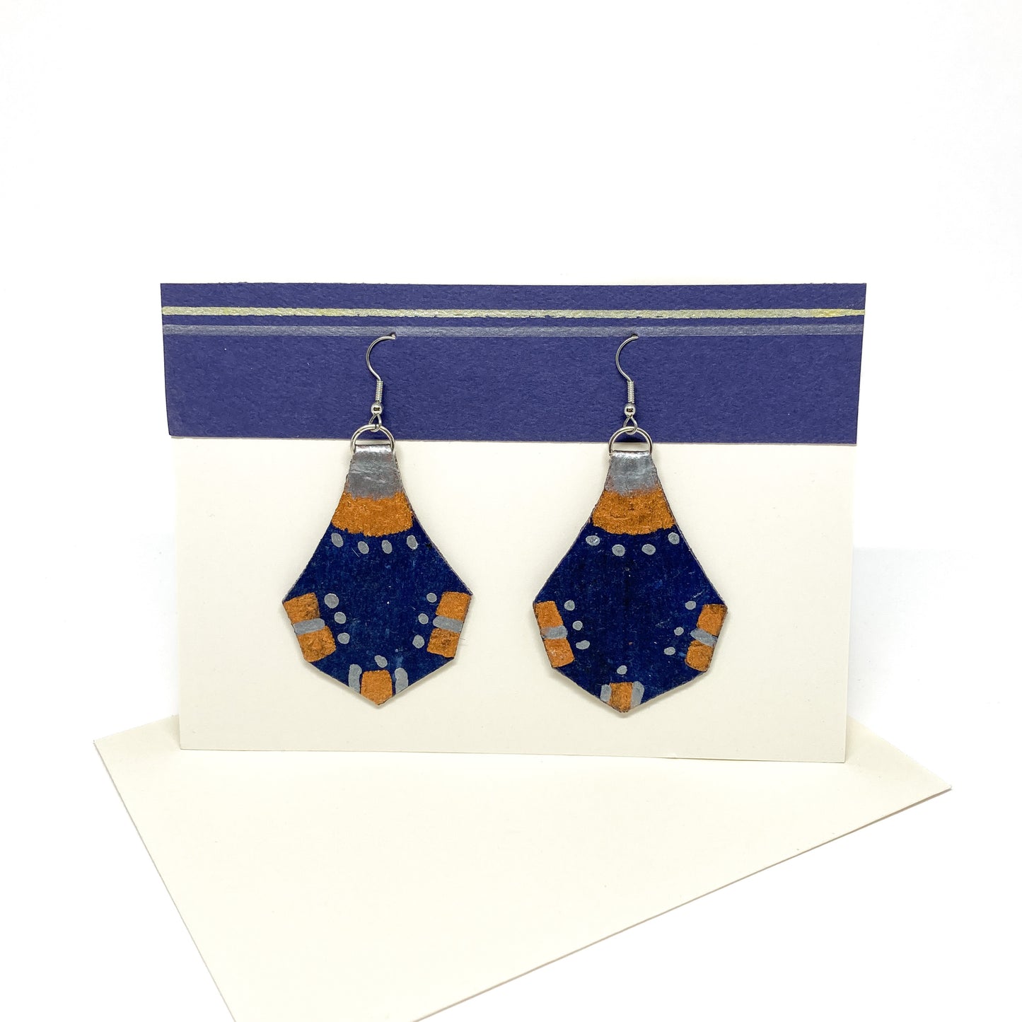 Two blue, copper, and silver geometric earrings with a unique hexagonal shape and dotted details hang from silver hooks.