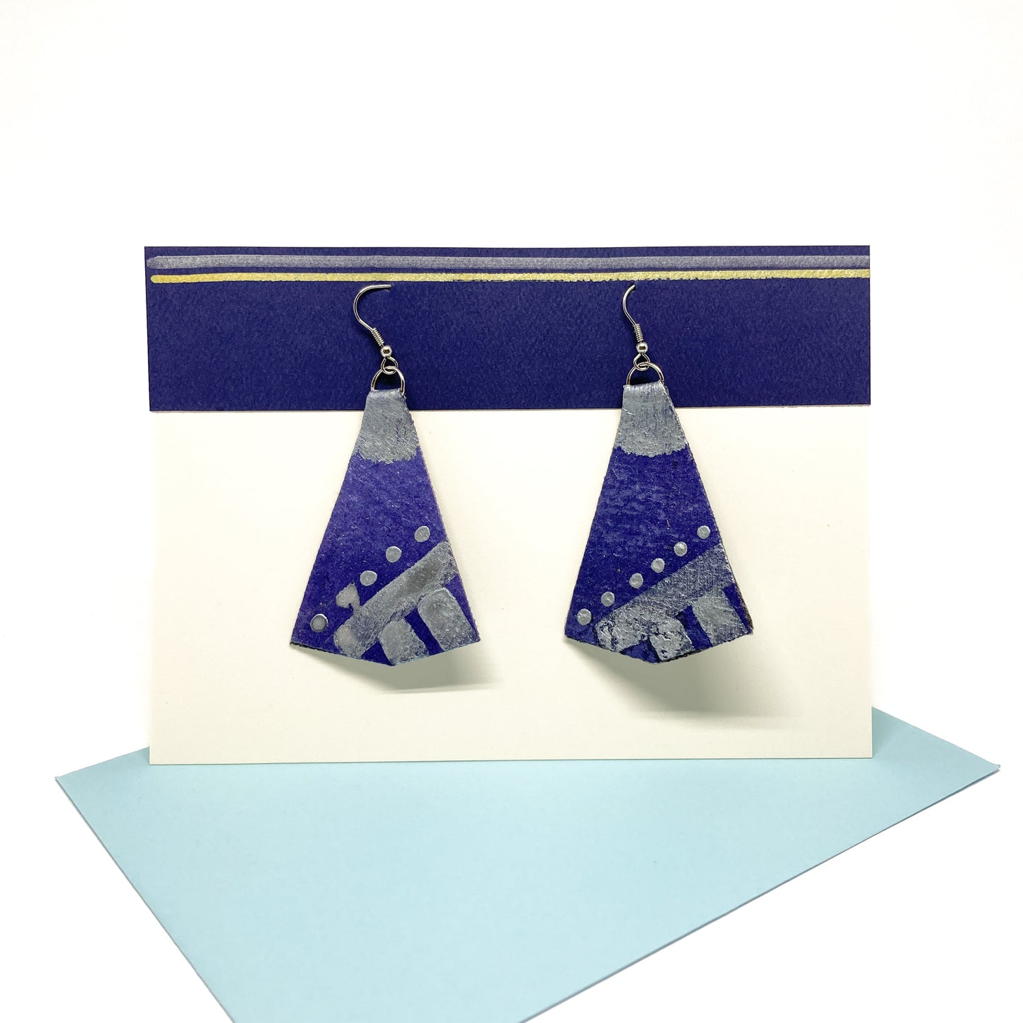 Two purple, silver, and white geometric earrings hang from silver hooks on a display card.