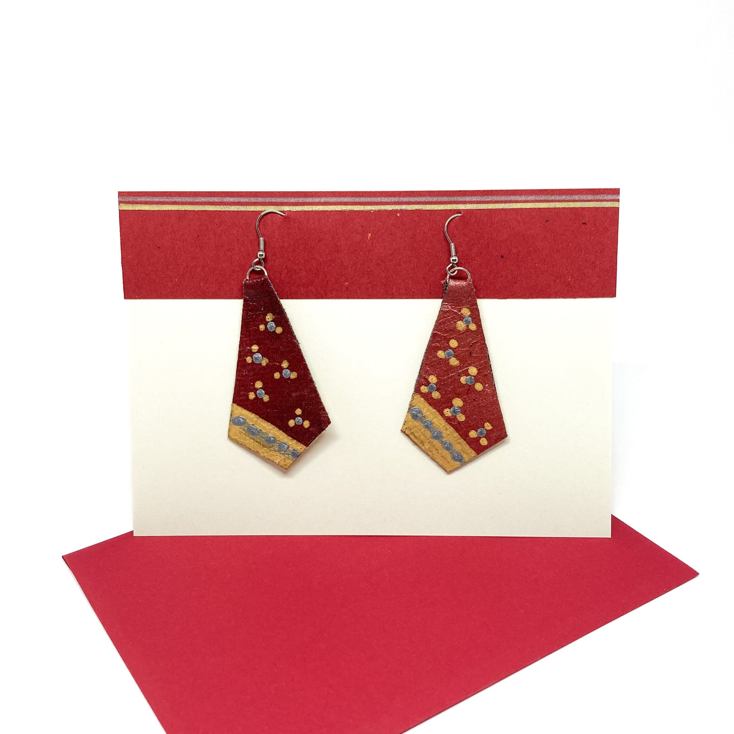 Red diamond earrings with gold and blue accents displayed on a white card with red and gold stripes, atop a red card.