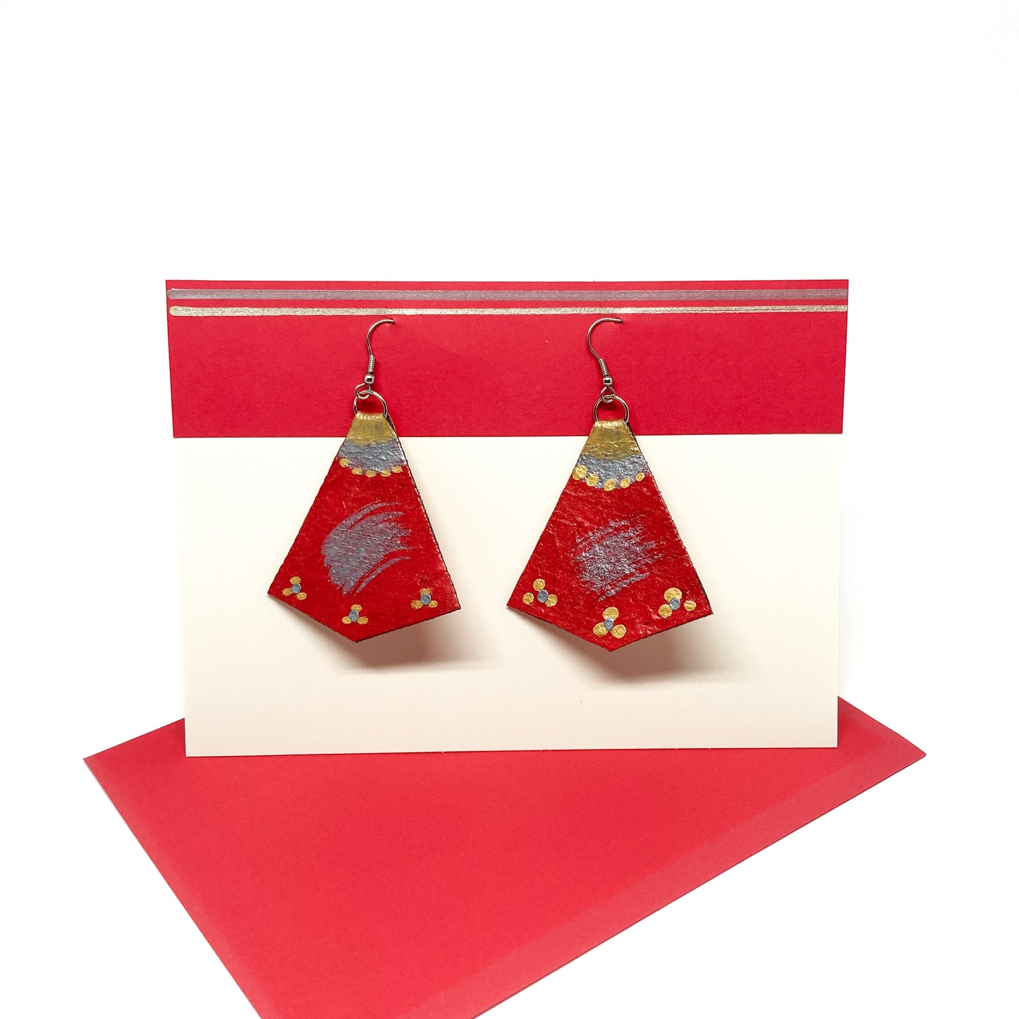 Two red, gold, and silver geometric earrings hang from silver hooks on a display card.