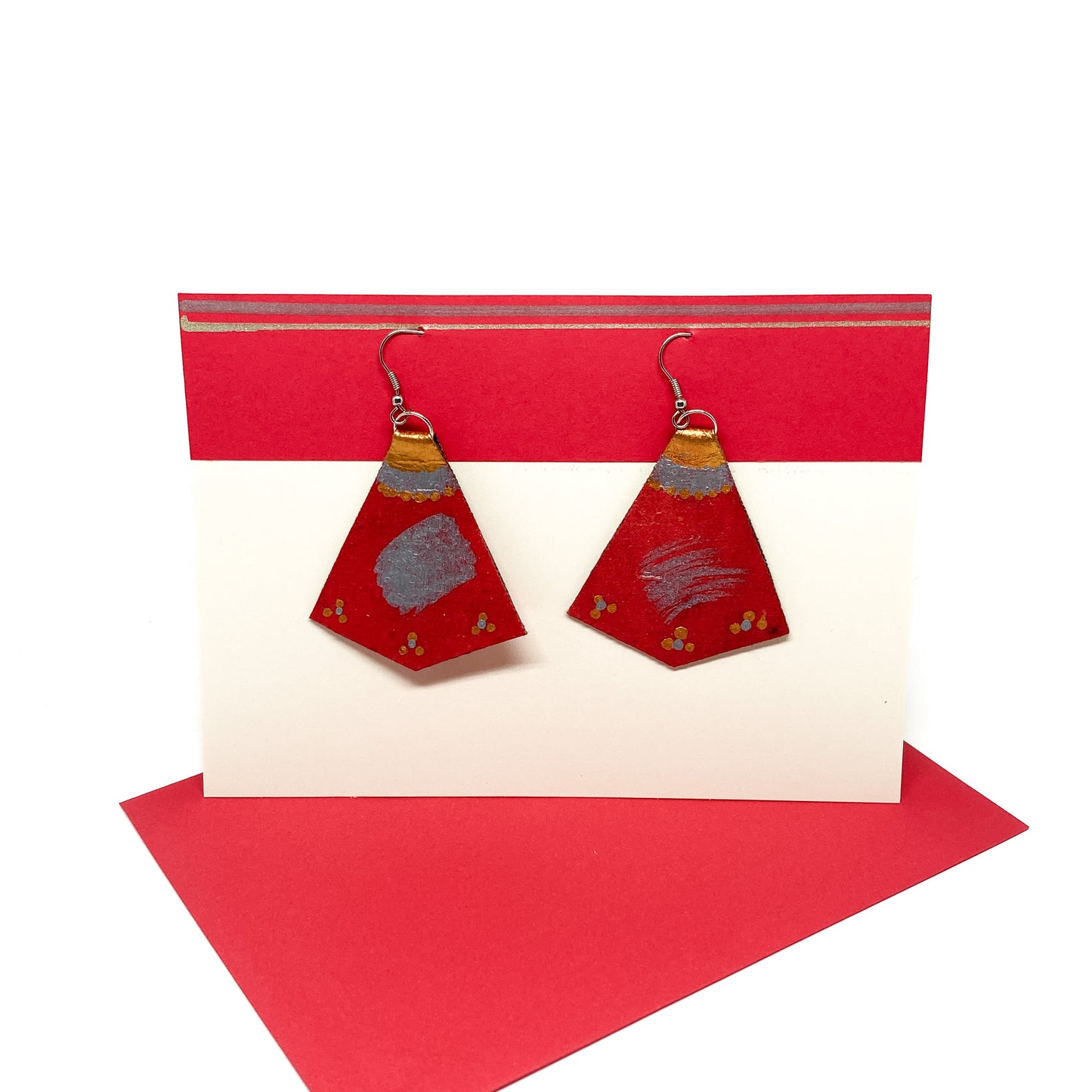 Two red, gold, and silver geometric earrings with unique designs hang from silver hooks on a display card.