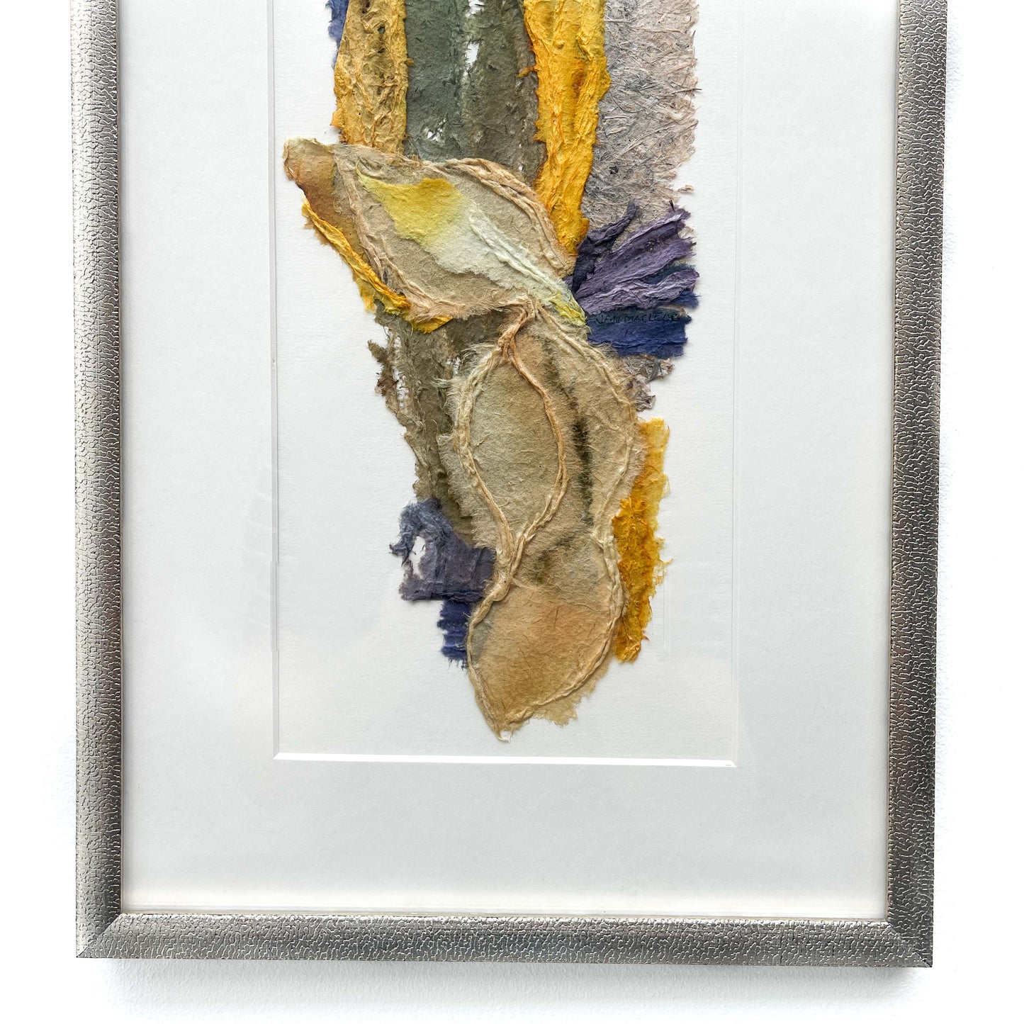 Close-up of framed abstract textile art with layered textures and blended hues of yellow, blue, green, brown, and gray.