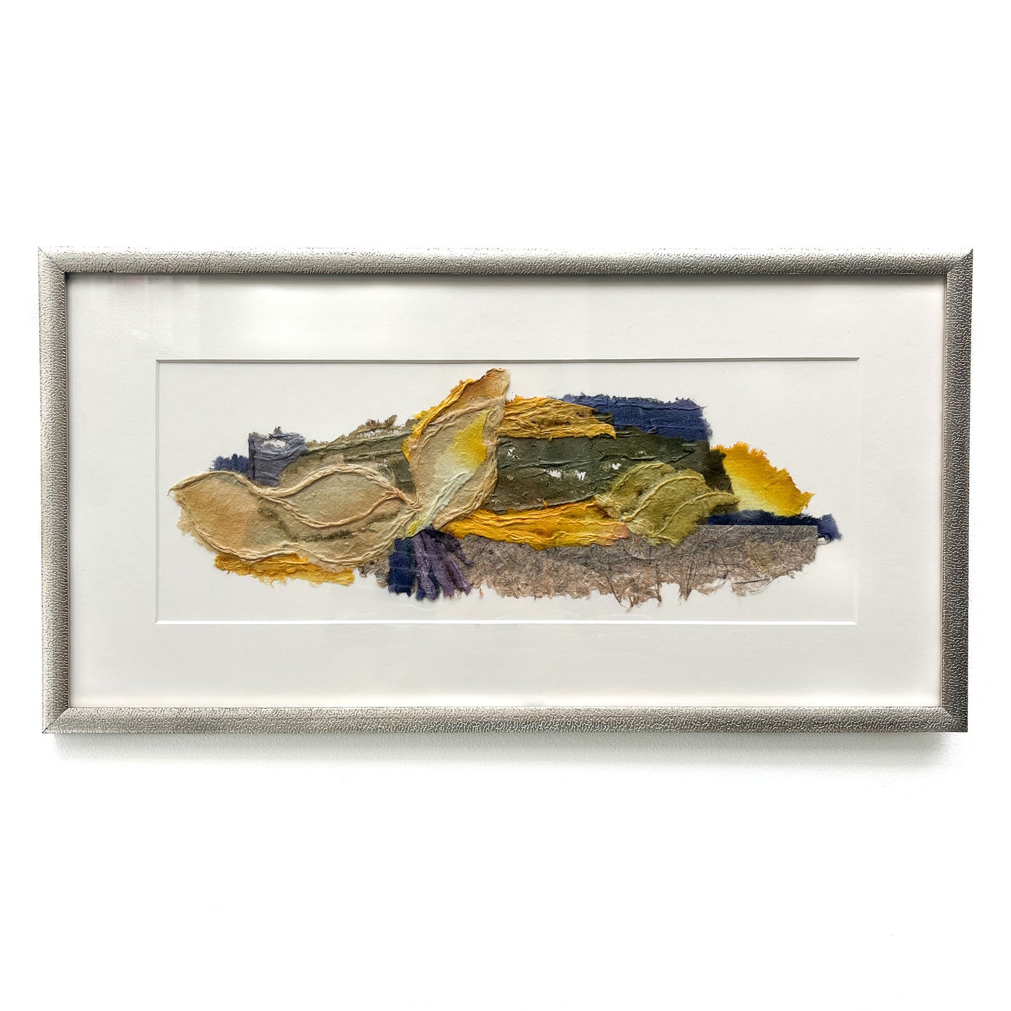 Framed horizontal abstract textile art with layered textures and blended hues of yellow, blue, green, brown, and gray.