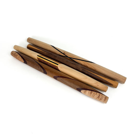 Five wooden rolling pins with various wood grains and decorative accents, arranged diagonally. The rolling pins have a smooth, polished finish.