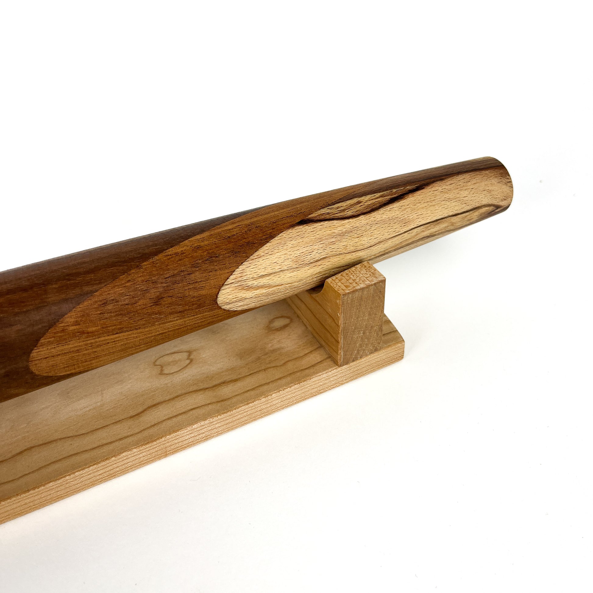 A close-up of a wooden rolling pin with a unique design, resting on a wooden stand. The rolling pin has a smooth, polished finish.