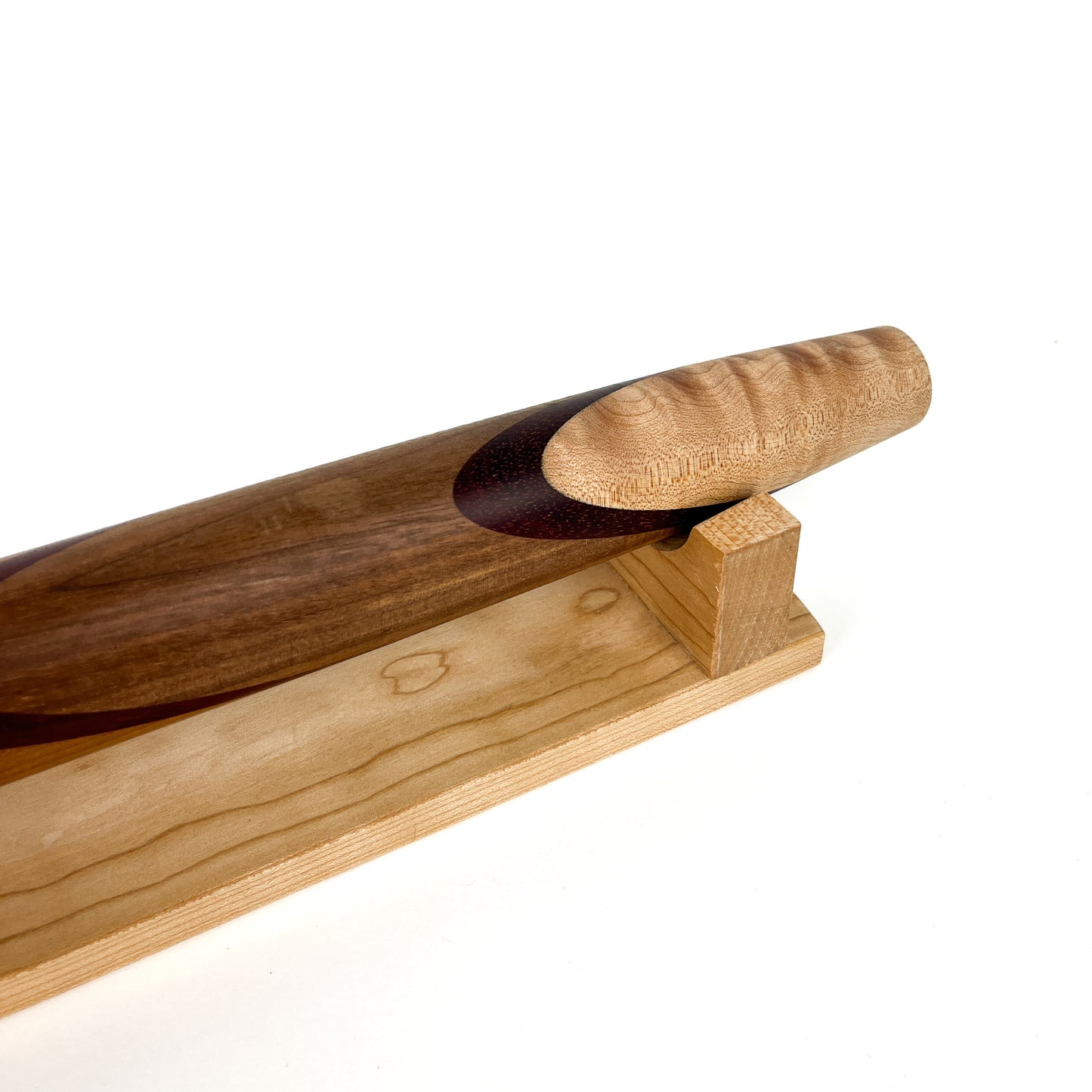 A close-up of a wooden French rolling pin with a unique design, resting on a wooden stand. The pin has a smooth, polished finish.