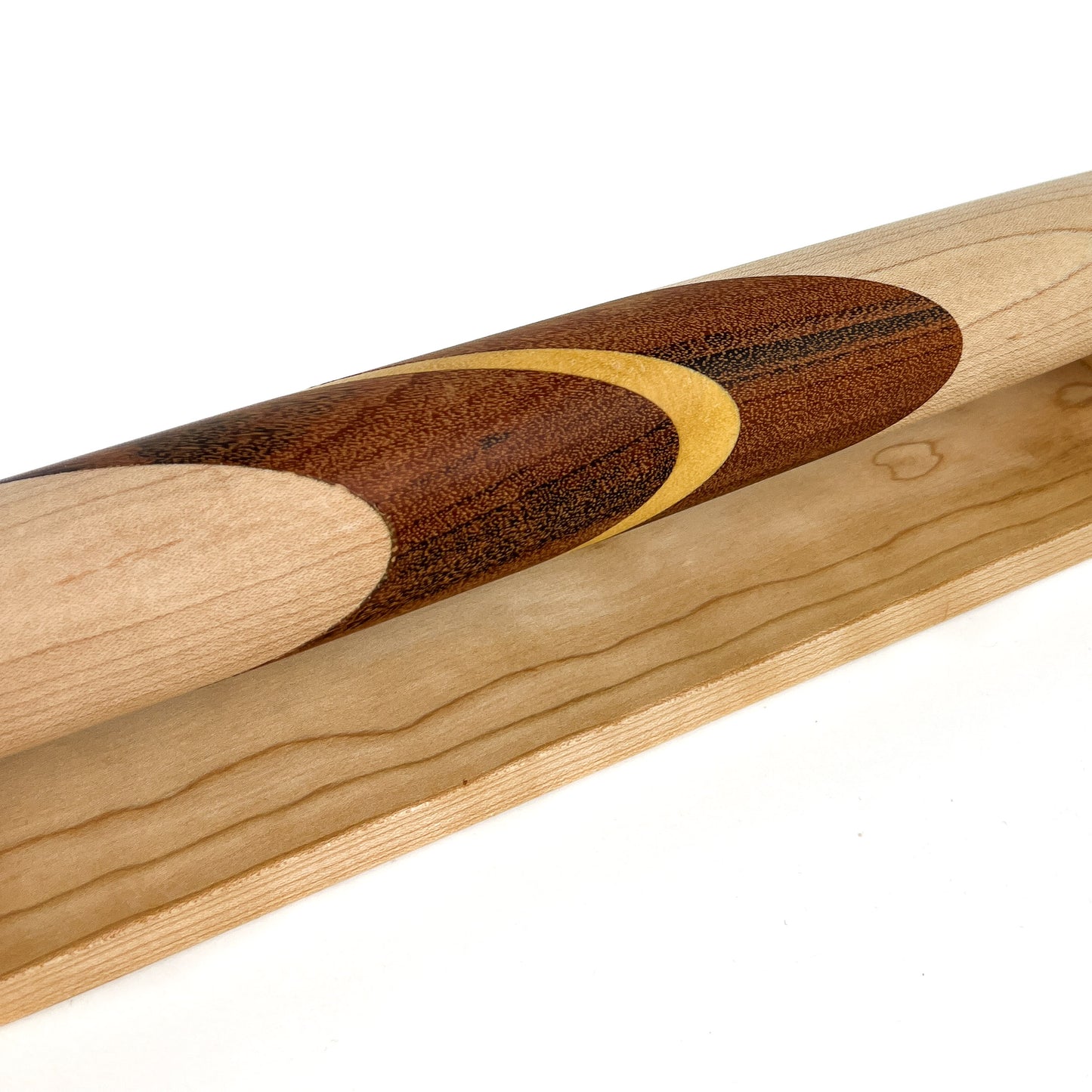 A close-up of a wooden French rolling pin with a crescent moon inlay, resting on a wooden stand. The pin has a smooth, polished finish.