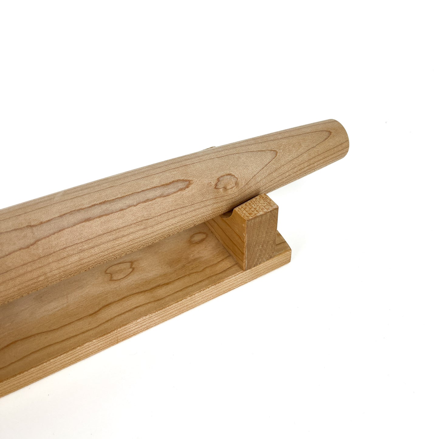 A close-up of a light-colored wooden French rolling pin resting on a wooden stand. The pin has a smooth, polished surface.