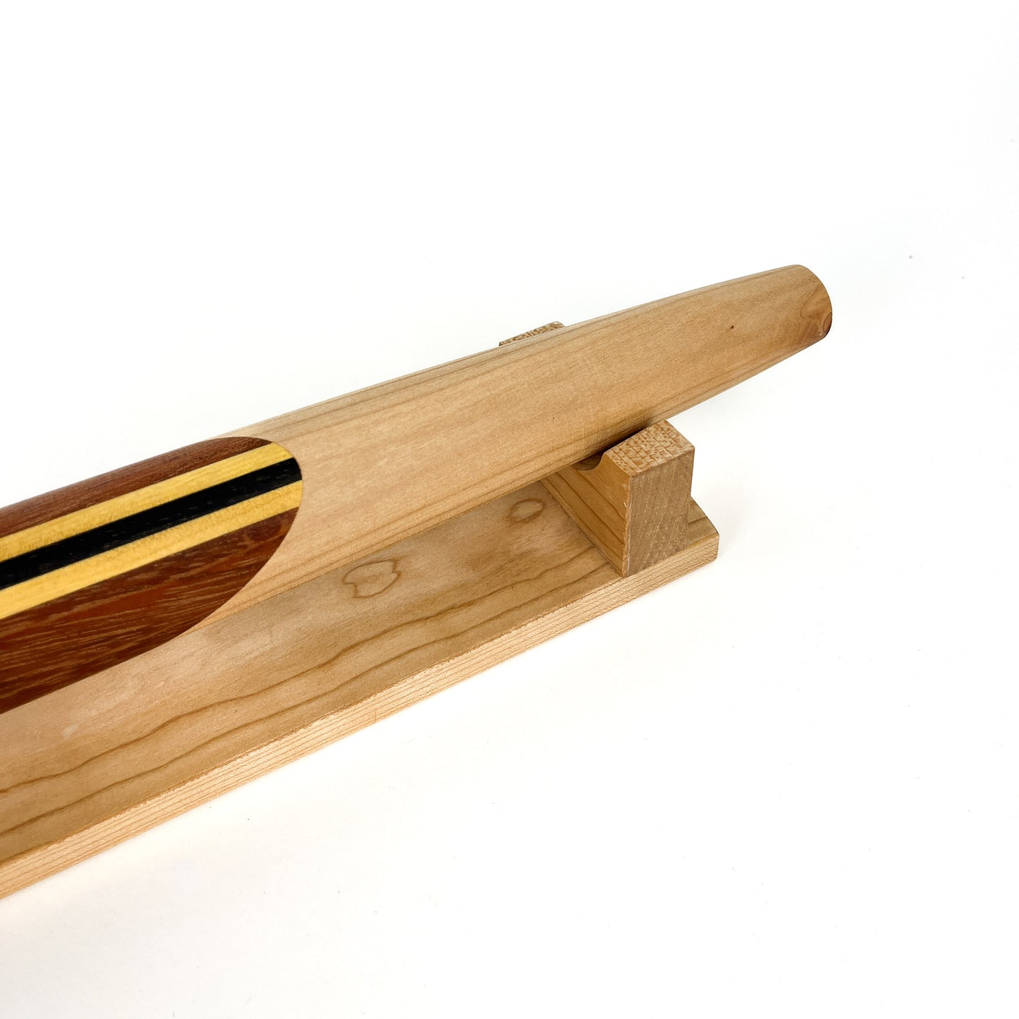 A close-up of a wooden French rolling pin with a decorative striped inlay, resting on a wooden stand. The pin has a smooth, polished finish.