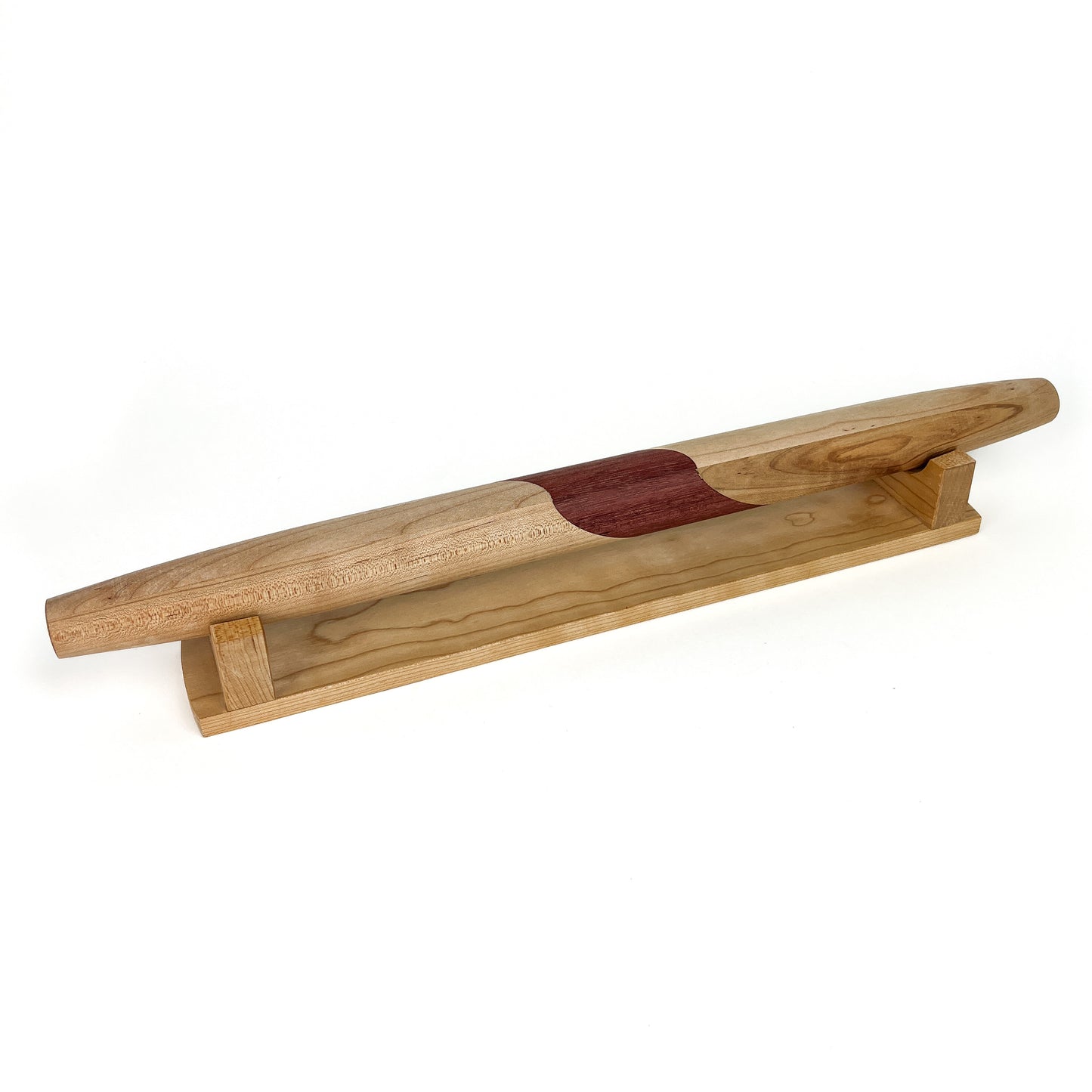 A wooden French rolling pin with a dark, curved inlay, resting horizontally on a light-colored wooden stand. The pin has a smooth finish.