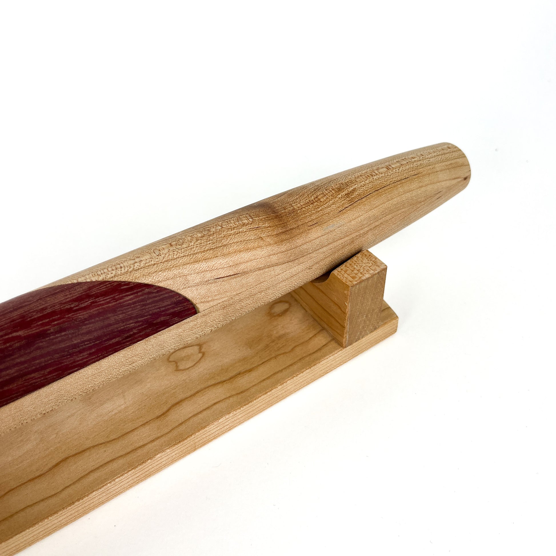 A close-up of a wooden French rolling pin with a dark inlay, resting on a wooden stand. The pin has a smooth, polished finish.