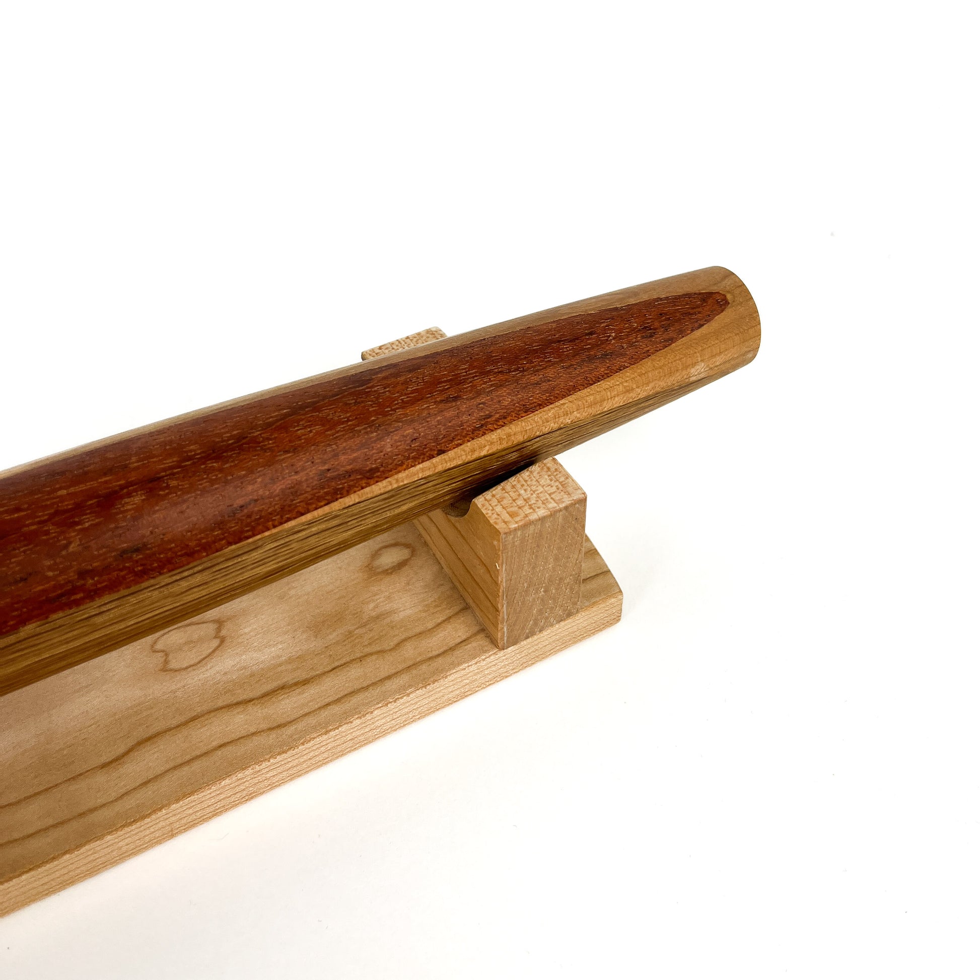 A close-up of a French rolling pin made of Jatoba wood, resting on a Sugar Maple stand. The pin has a smooth, polished finish.
