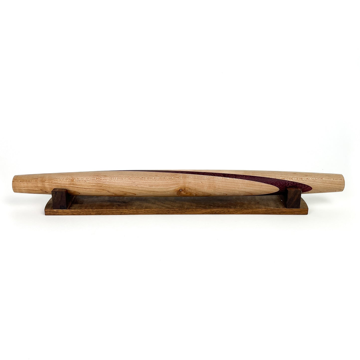 A wooden French rolling pin with a dark purple inlay, resting on a dark wooden stand. The pin has a smooth, polished finish.