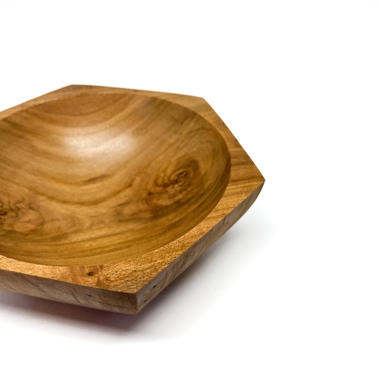 A close-up of a six-sided wooden bowl with visible grain and a smooth, carved interior. The bowl has a shallow depth.