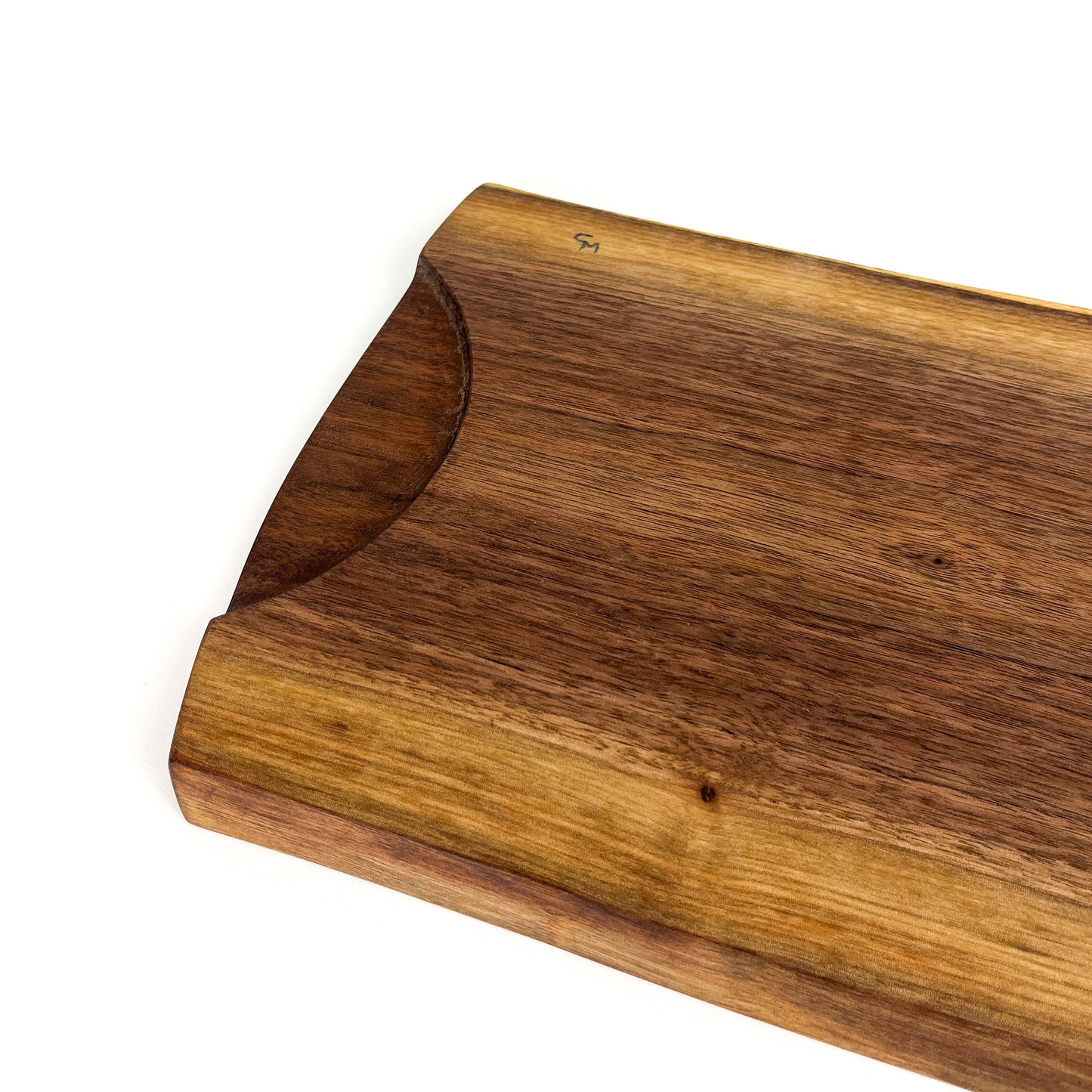 Angled close-up of a live edge wooden board with an integrated handle and natural wood markings.