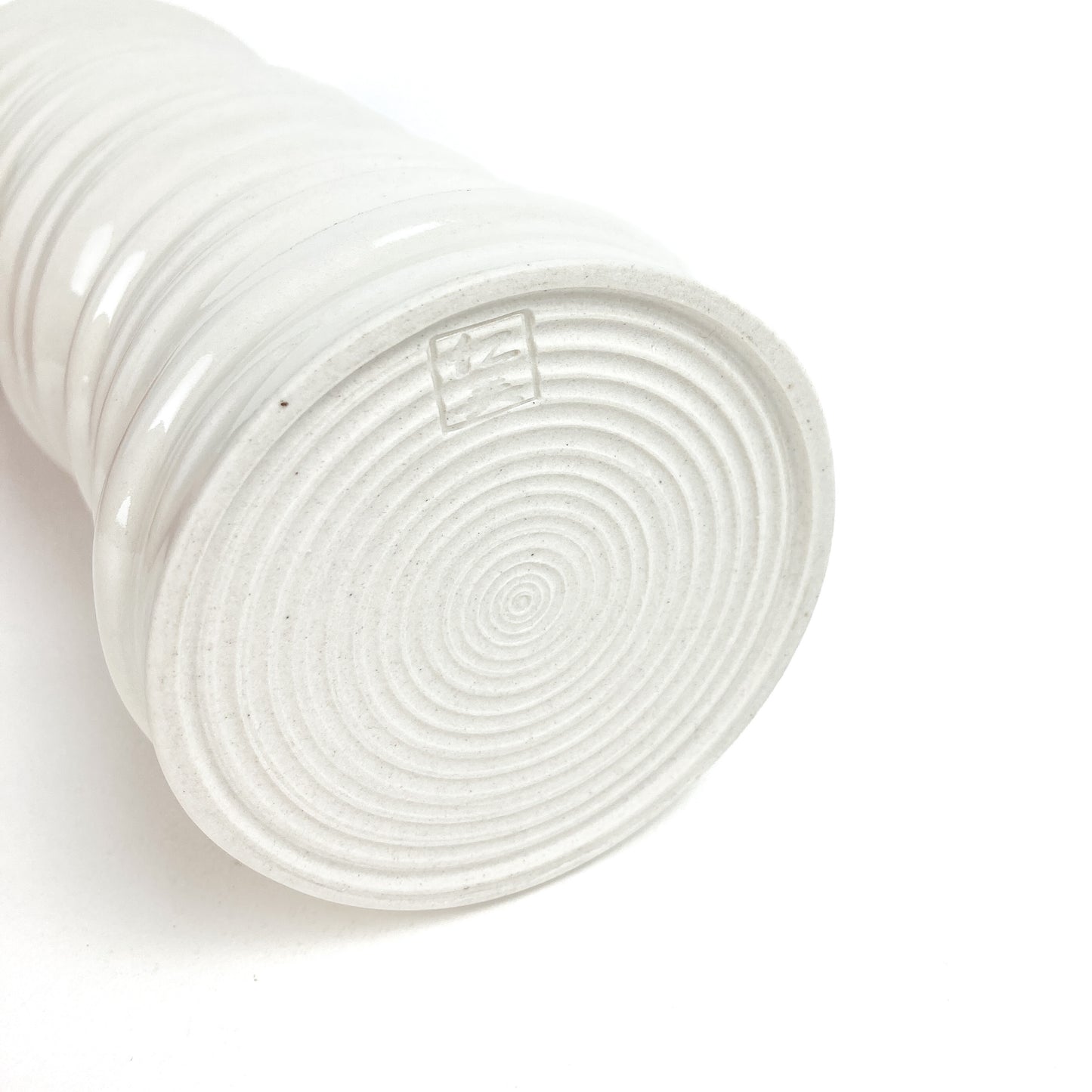Bottom view of a ceramic vase showing concentric circular markings and a small, square maker's mark. The vase has textured horizontal ridges.