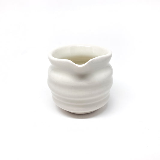 A small, round ceramic creamer with horizontal ridges and a pointed spout on one side.