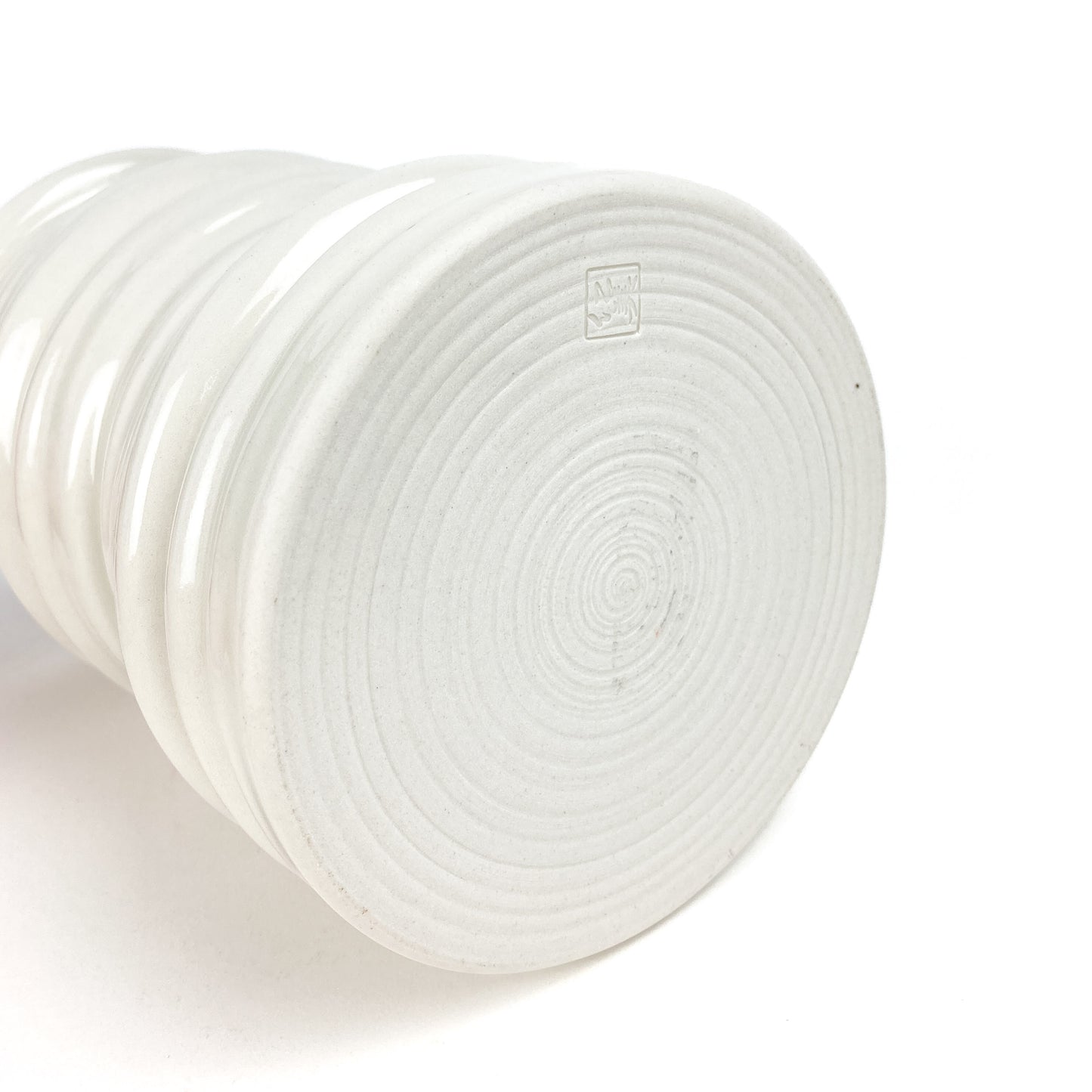 Bottom view of a ceramic Yunomi cup showing concentric circular markings and a small, square maker's mark. The cup has textured horizontal ridges.