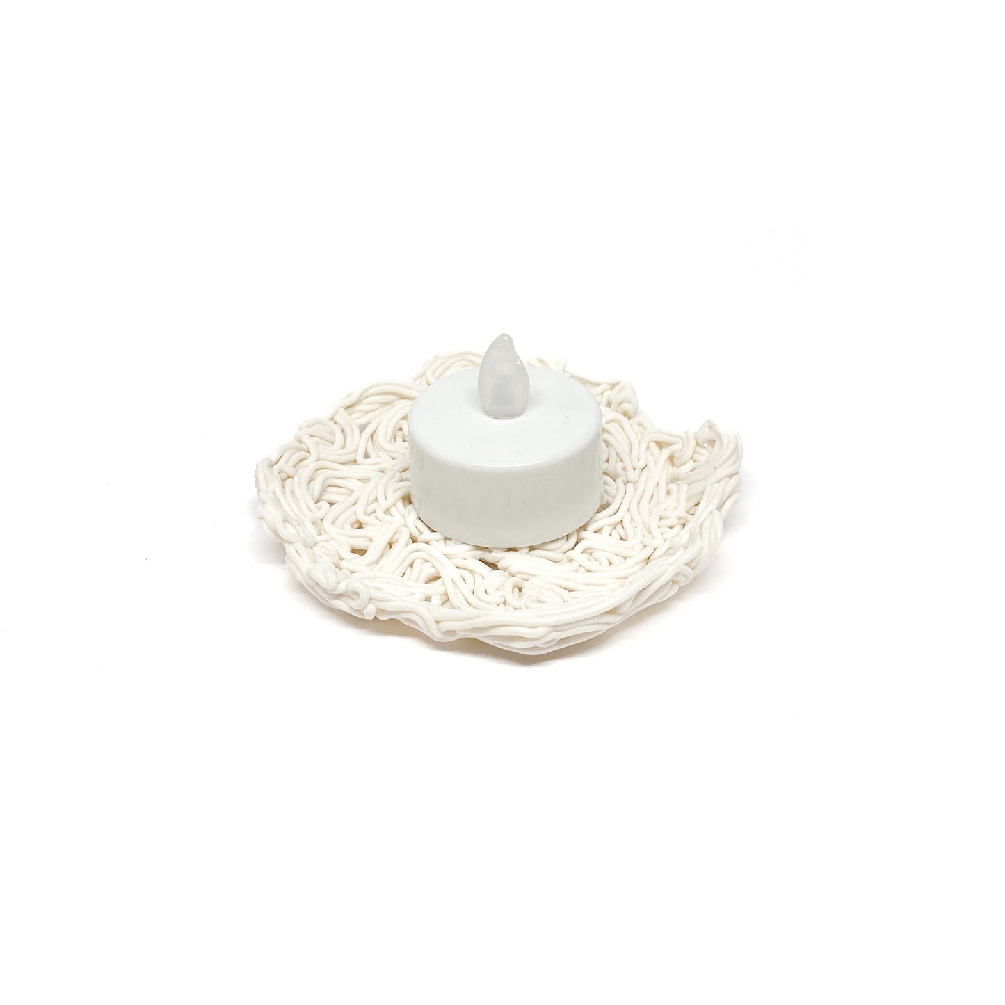 A small, round LED candle sitting on a textured, shallow ceramic dish resembling tangled strands or noodles.