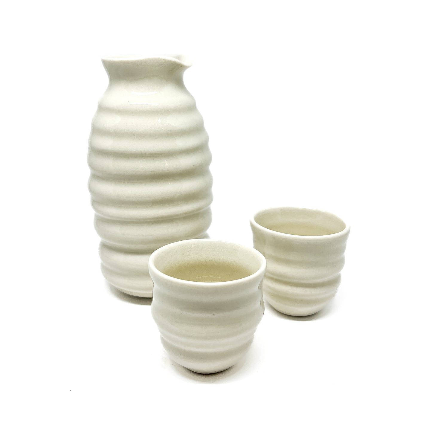 A ceramic sake set with a ridged bottle and two small, ridged cups, one filled with liquid.