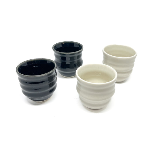 Four small ceramic Yunomi cups, two dark and two light, each with horizontal ridges around the body.