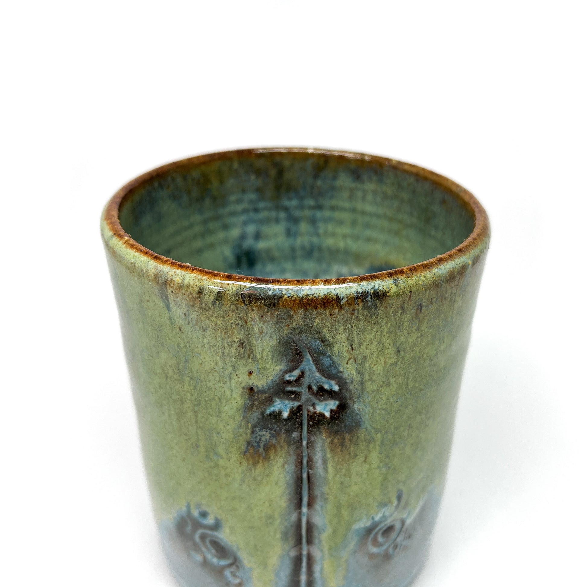 Closeup glazed terracotta cup with tree design.