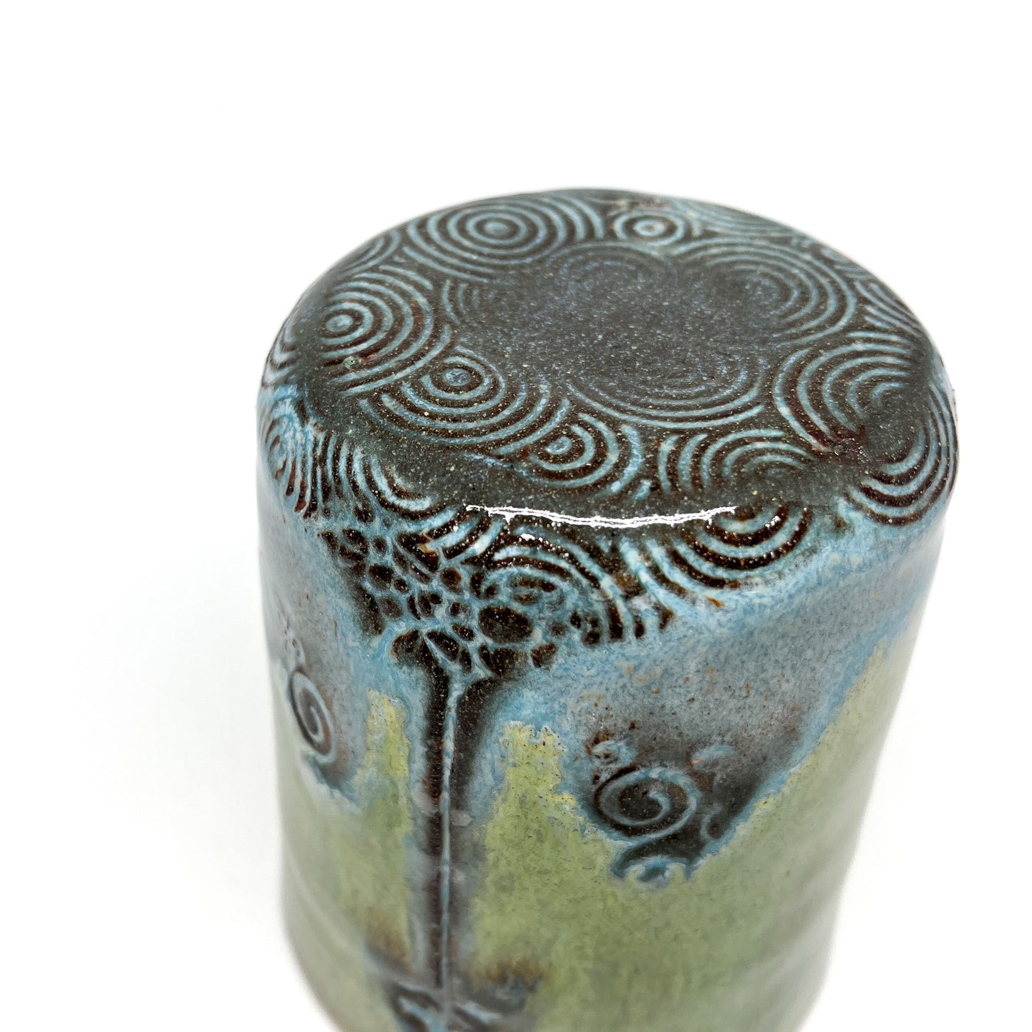 Close-up of a green ceramic cup with tree design and spiral pattern on top, isolated on white.