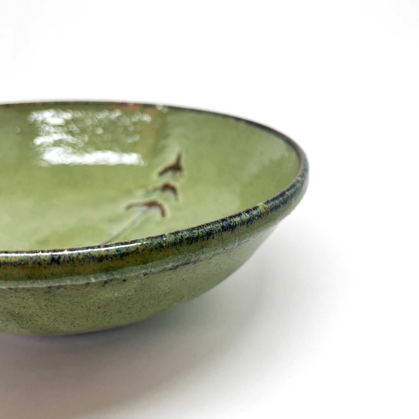 Close-up of a green glazed terracotta bowl with a tree design, angled view on a white background.