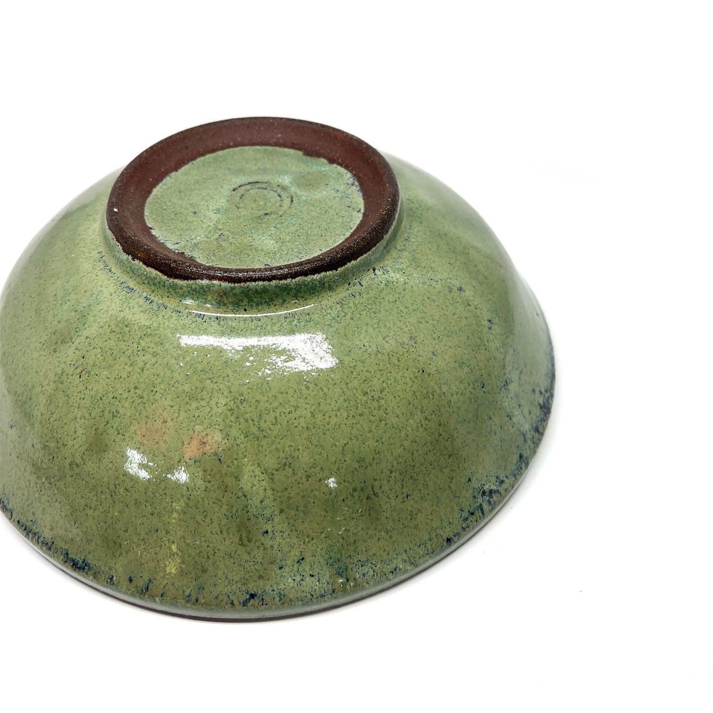 Underside of a green glazed terracotta bowl with a dark brown foot ring, angled view on a white background.