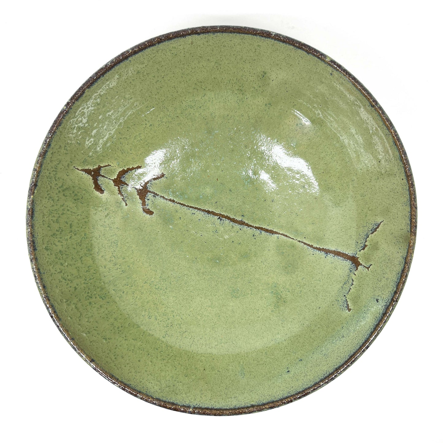 Green glazed terracotta plate with a tree design in the center, top-down view on a white background.