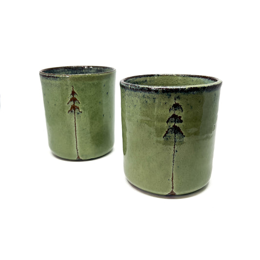 Two green ceramic cups with tree designs, isolated on a white background.