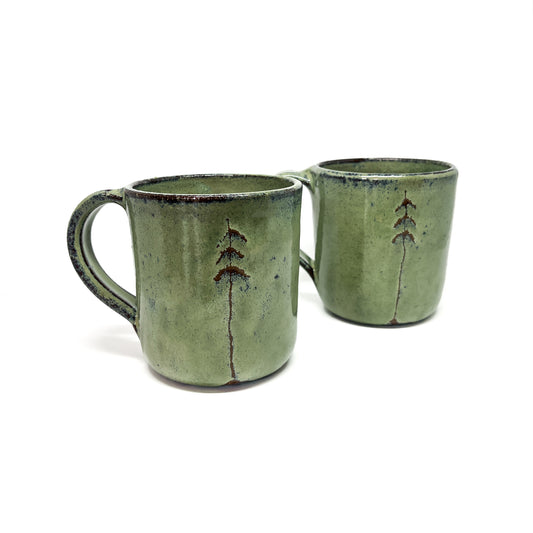 Two green ceramic mugs with tree designs.
