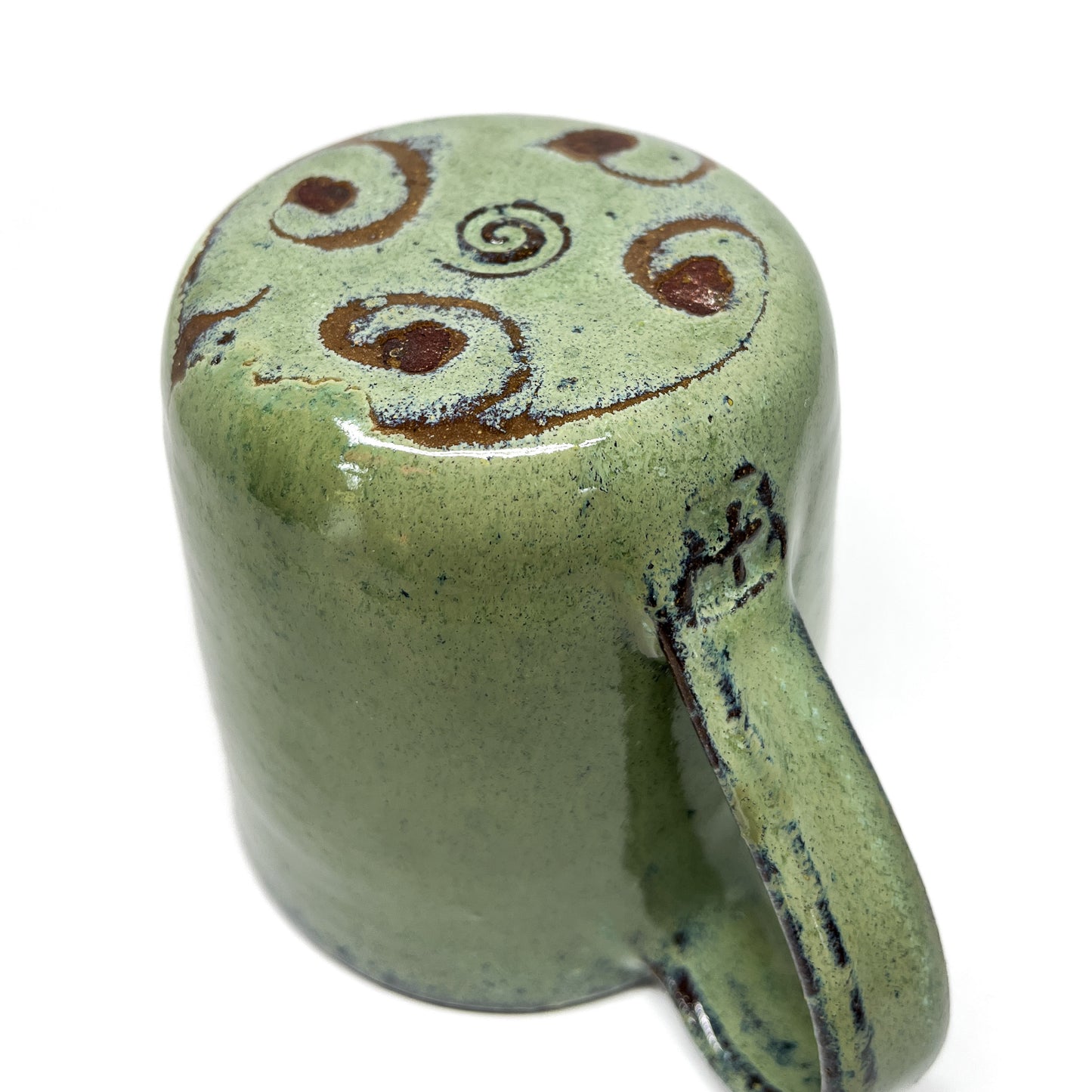 Green ceramic mug with brown spiral designs on top, angled view on a white background.