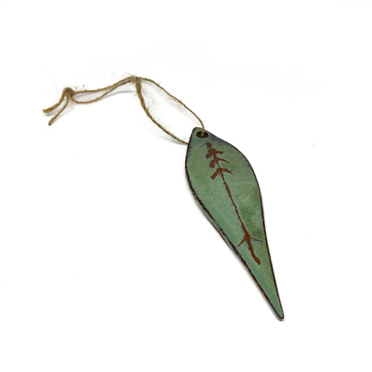 Green leaf-shaped ornament with tree design and twine.