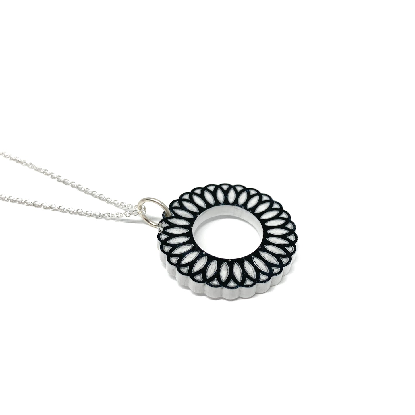 A silver chain necklace featuring a black and white circular pendant with an intricate, layered geometric design and a central open circle.